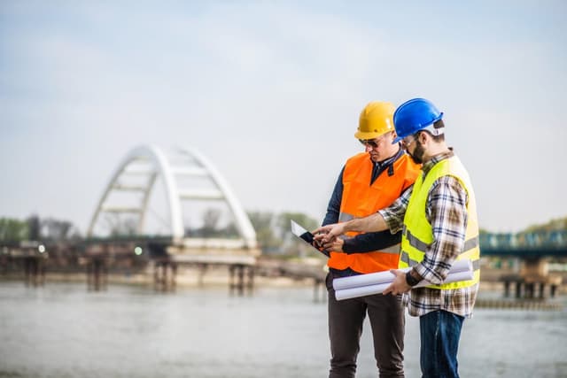 Two construction workers at a work site looking at an iPad 1200x801