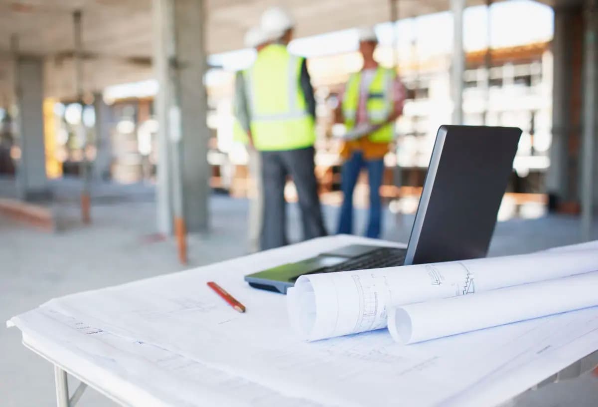 Drawings on a table and three construction workers in the background 1200x816